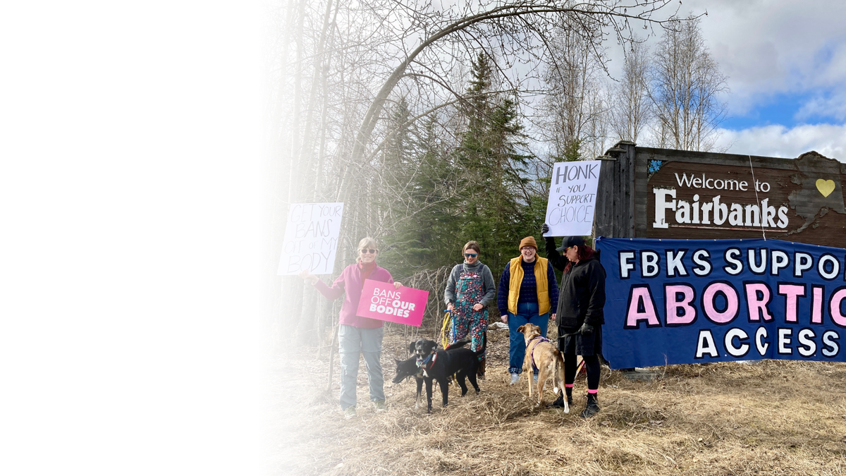 Planned Parenthood supporters hold pro-abortion signs in front of a City of Fairbanks sign